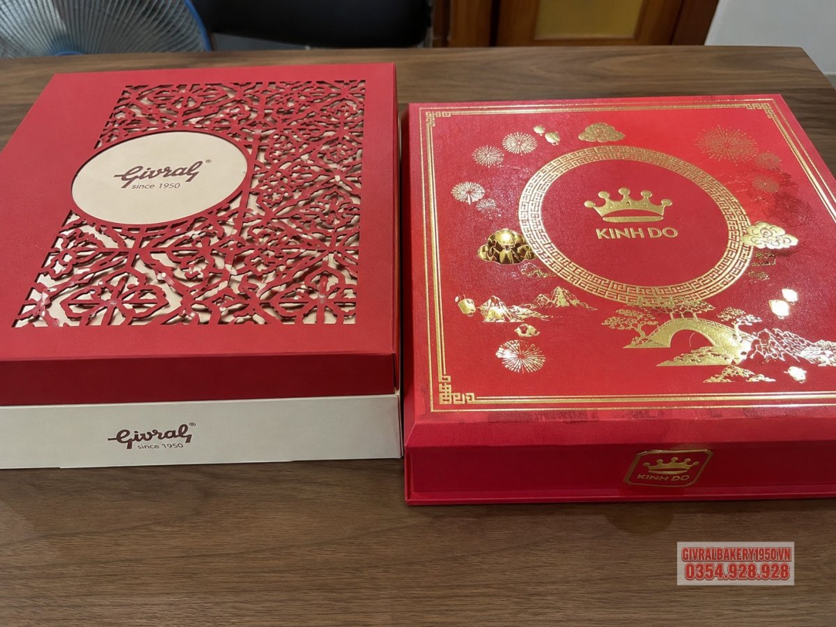 Cận cảnh hai mẫu hộp bánh trung thu Givral và Kinh Đô đặt cạnh nhau trên bàn gỗ, làm nổi bật sự khác biệt giữa phong cách sang trọng phương Tây và truyền thống phương Đông.